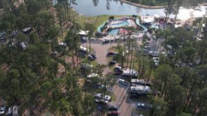 Aerial view of a Louisiana campground with RV sites among pines, pools, a lazy river, and a lake
