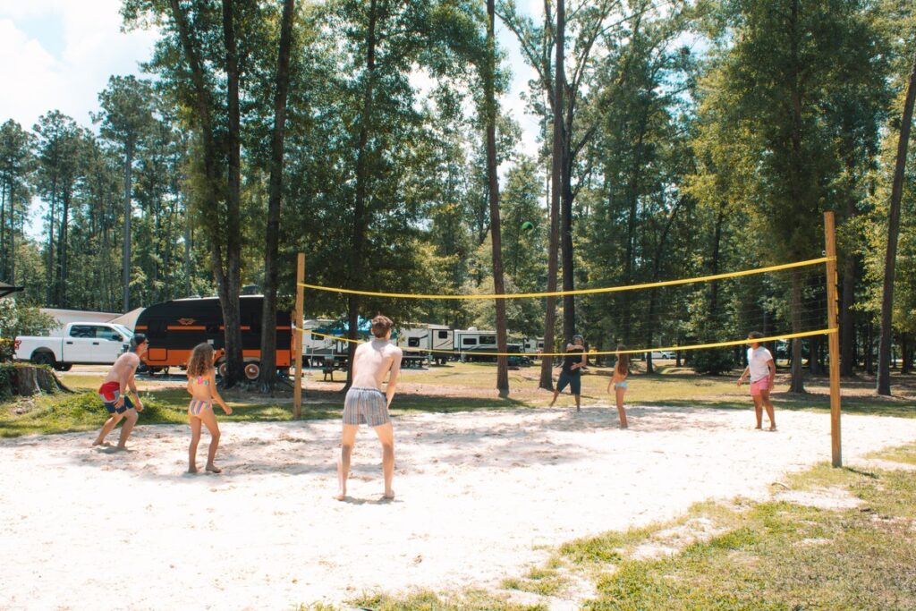 Guests playing sand volleyball among the pine trees at Fireside RV Resort in Ponchatoula, Louisiana.