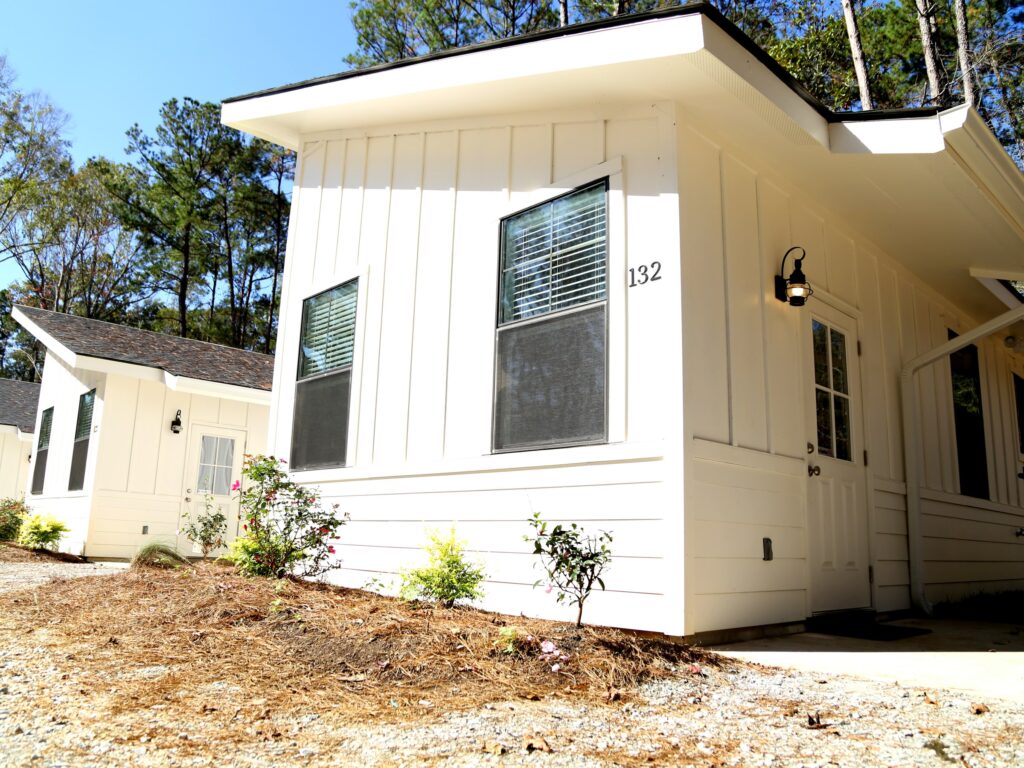 White board-and-batten rental cabin among tall pine trees at Fireside RV Resort in Ponchatoula Louisiana