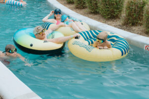 A family of five floats together on inflatable tubes down the lazy river at Fireside RV Resort on a sunny summer day