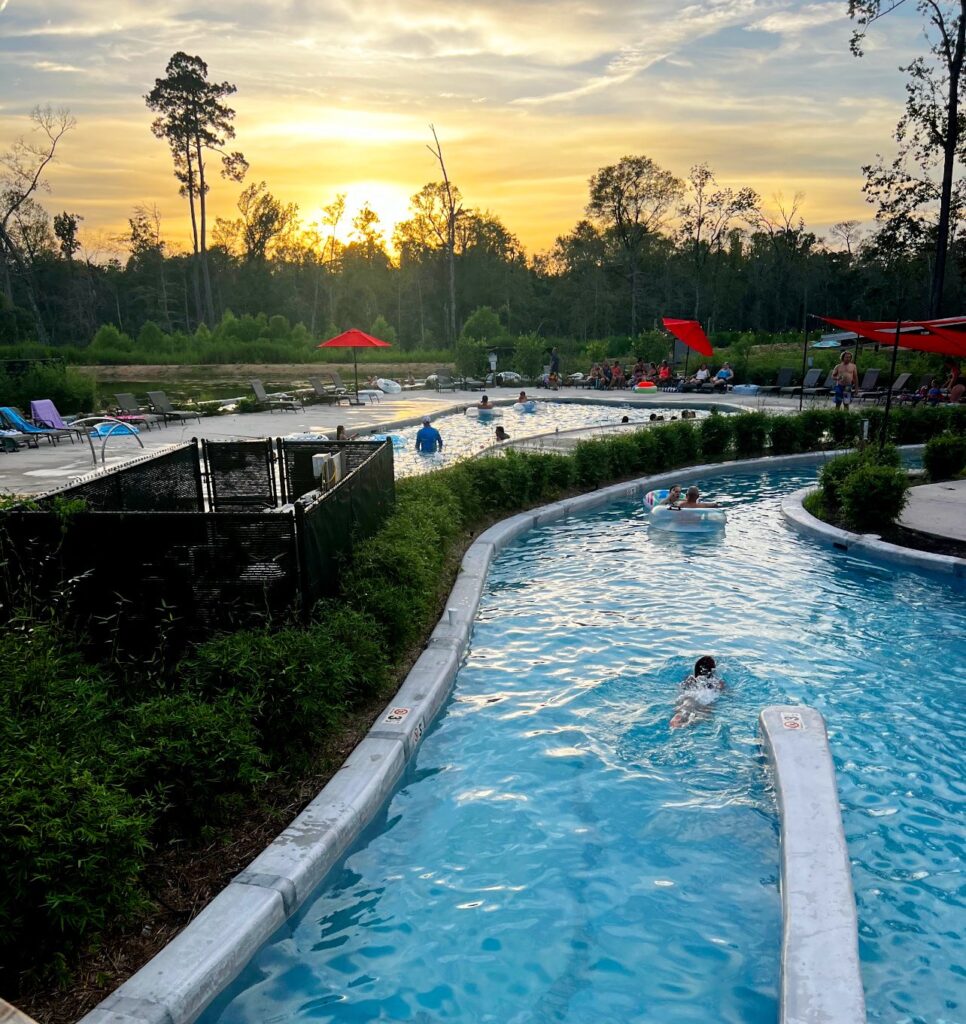 The winding lazy river at Fireside RV Resort at sunset, with guests floating on tubes past the pool deck and red umbrellas