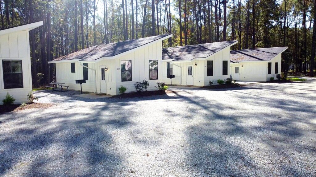 A row of modern, white, single-story cabins with distinctive asymmetrical gabled roofs sits along a wide gravel driveway at Fireside RV Resort in Ponchatoula, Louisiana.