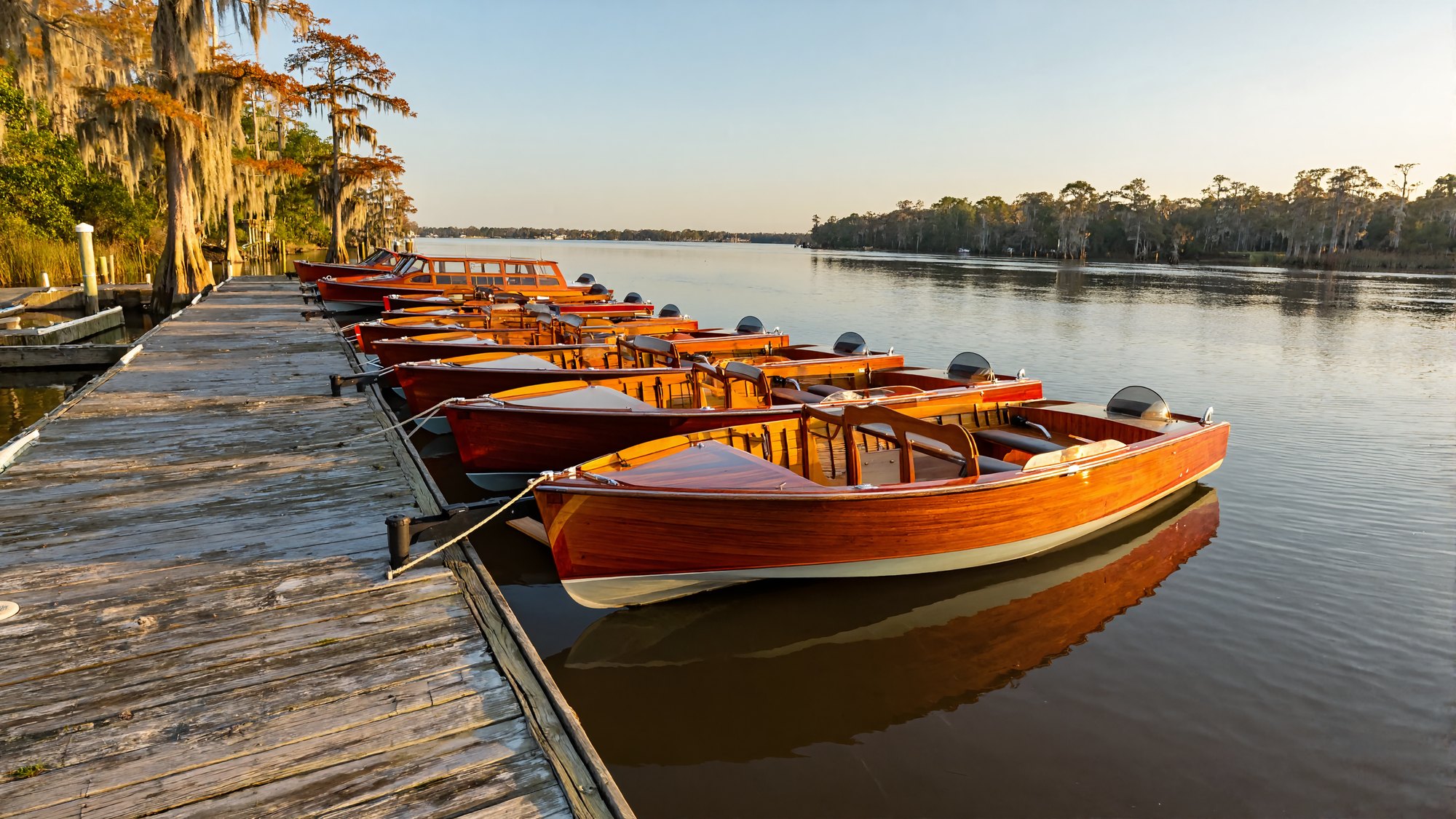 Classic varnished wooden boats moored along a tree-lined Louisiana river at golden hour