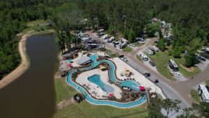 Aerial view of Fireside RV Resort near New Orleans showing the lazy river, pools, lake, and RV sites among pine trees in summer